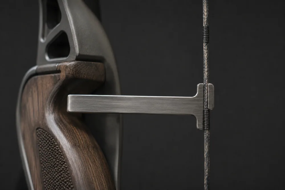 Close-up of a T-shaped bow square clipped to a recurve bowstring, measuring brace height to the grip throat.