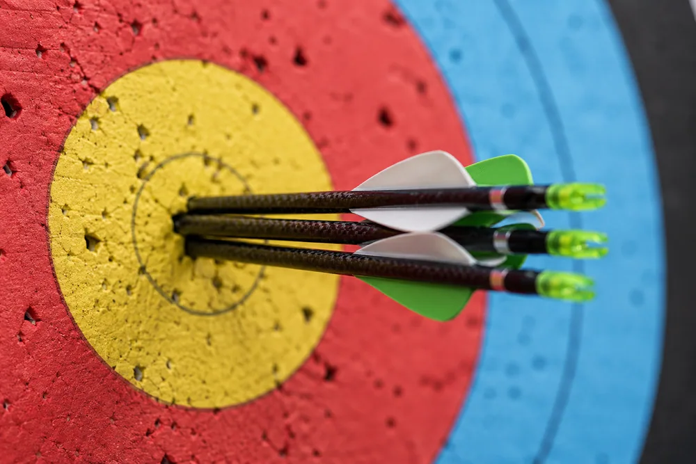 Three target arrows grouped tightly together in the yellow centre of a colourful archery target face.