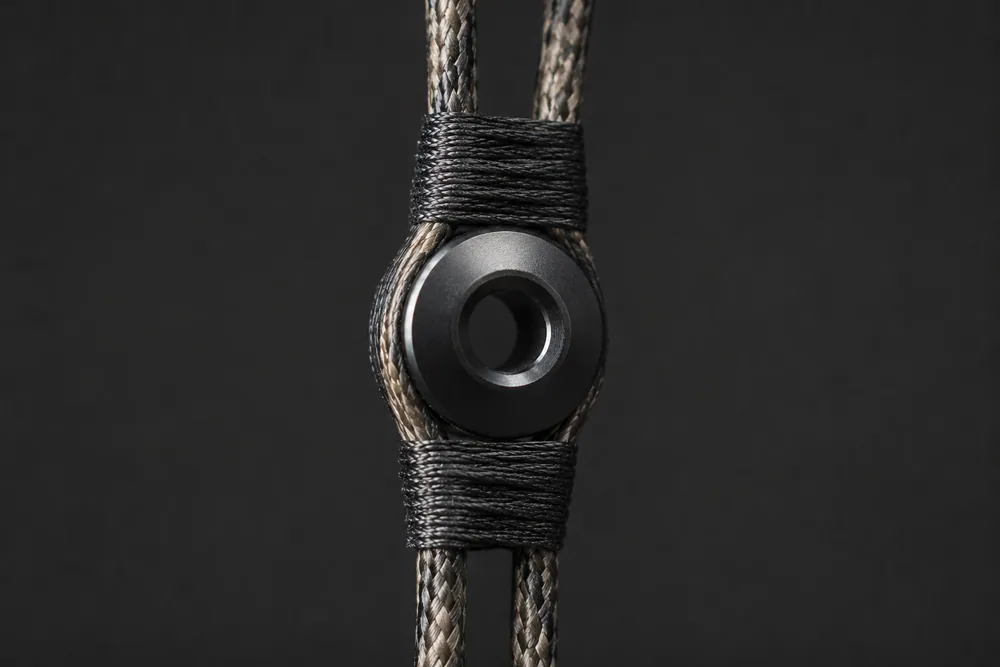 Close-up of a round aperture peep sight seated between the strands of a bowstring, held by serving thread above and below.